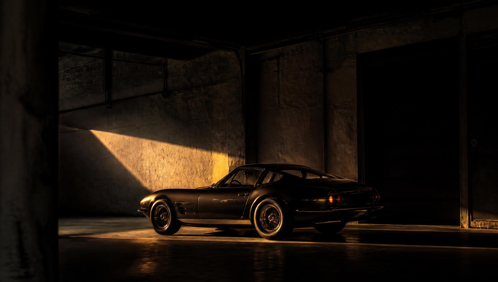 Rare classic coupe lit by a single warm light in a dark warehouse